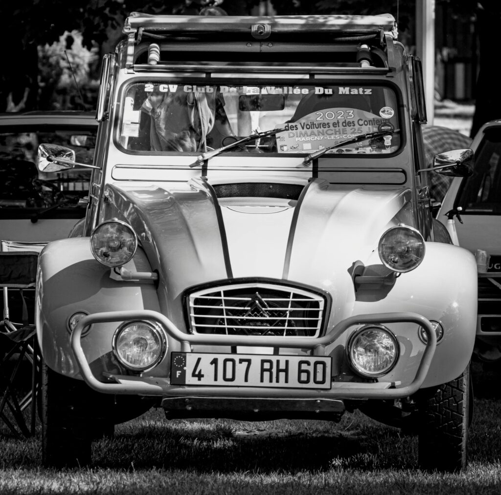Black and white image of a vintage Citroen 2CV parked at an outdoor motor show.