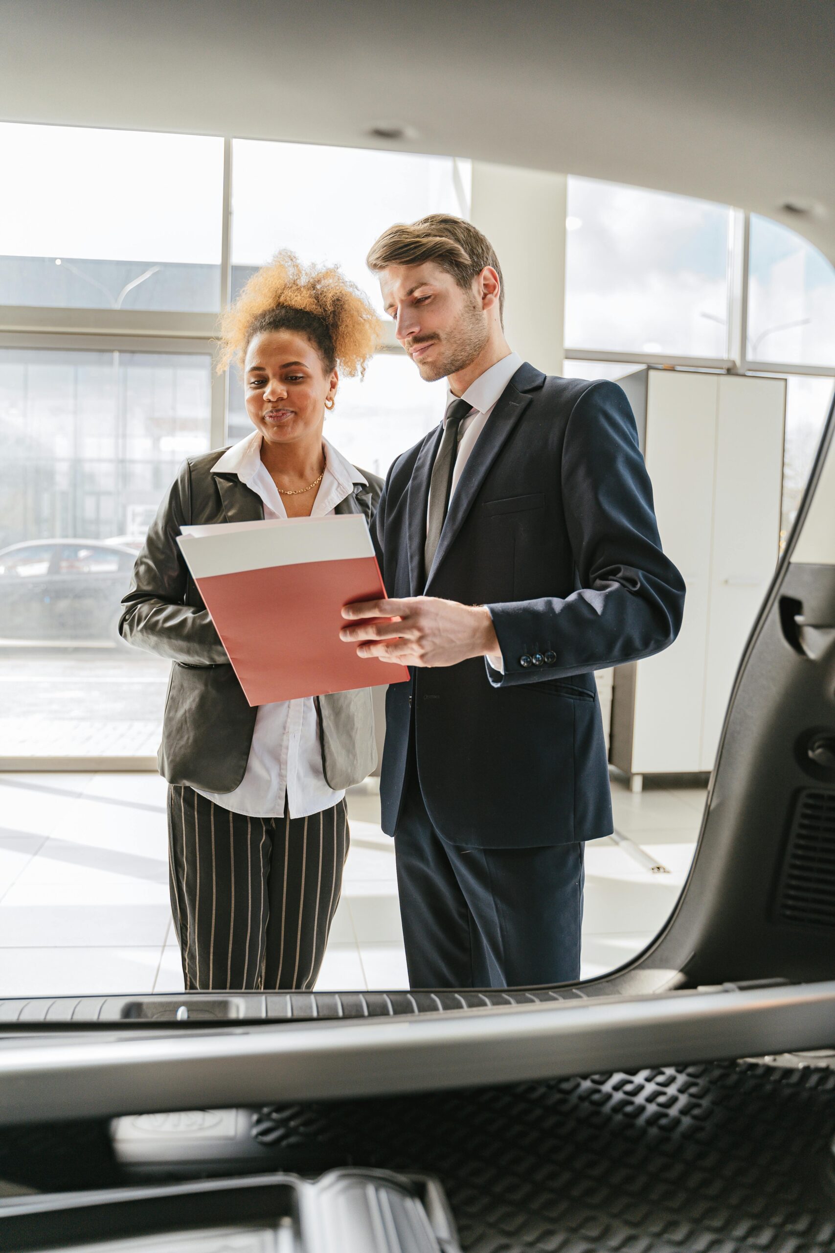 Man and woman discussing car details in showroom, professional sales consultation.