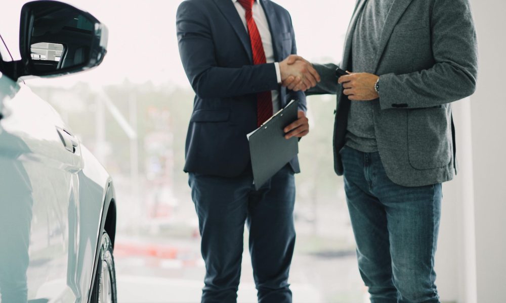 Two men shake hands in a car dealership, sealing a business deal.