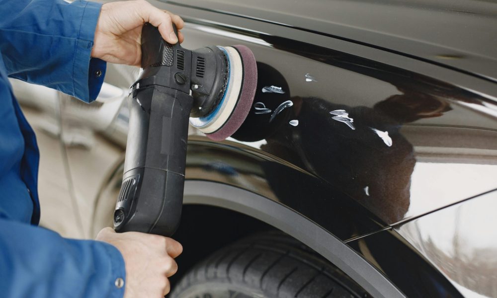 Hands using a polishing machine on a car's surface in a garage setting.