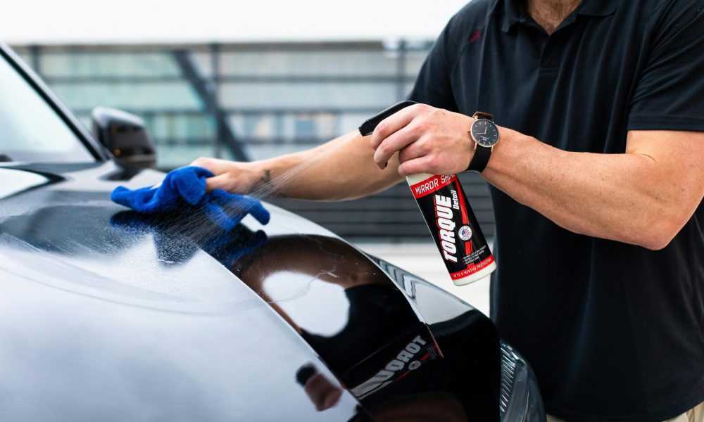 A man cleaning a black car hood with a spray and microfiber cloth.